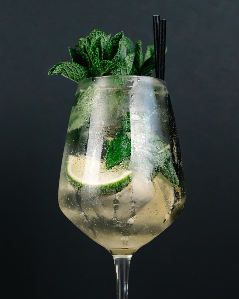 Hugo Spritz cocktail in a wine glass with mint and lime garnish.