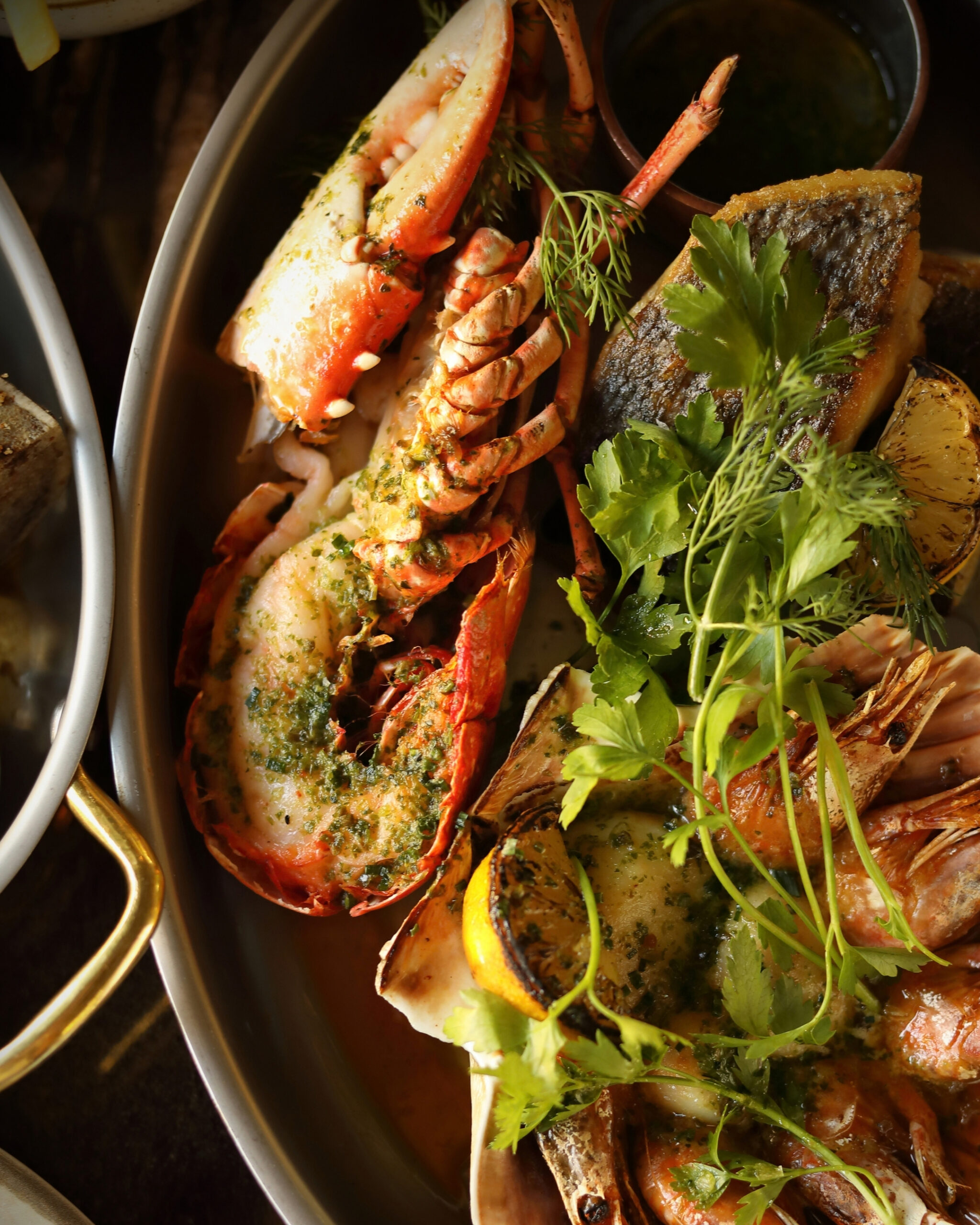 http://Seafood%20platter%20with%20lobster%20tails,%20shrimp,%20grilled%20fish,%20and%20fresh%20parsley%20on%20a%20metal%20serving%20dish.