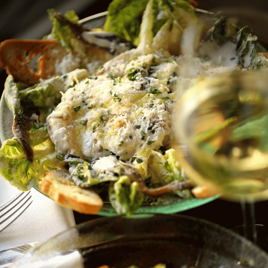 http://Plate%20of%20creamy%20herb-crusted%20chicken%20on%20a%20bed%20of%20greens%20with%20croutons%20and%20grated%20cheese,%20with%20a%20glass%20of%20white%20wine%20nearby.